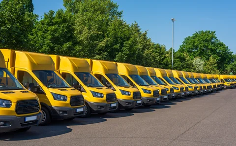A fleet of electric yellow delivery vans are parking in front of green trees