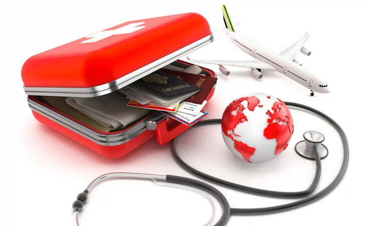 First-aid kit designed as a suitcase with passports, plane tickets and clothes inside, stethoscope and globe isolated on white. Medical tourism concept.