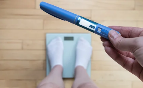 Ozempic Insulin injection pen for diabetics and weight loss. Woman weighs herself and holds Ozempic in her hand. Weight loss concept.