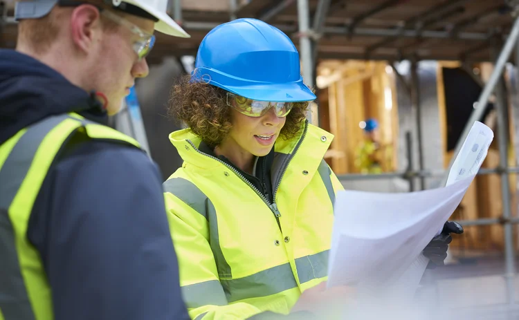 a female construction worker stands on a building site housing development and instructs a co -worker.
